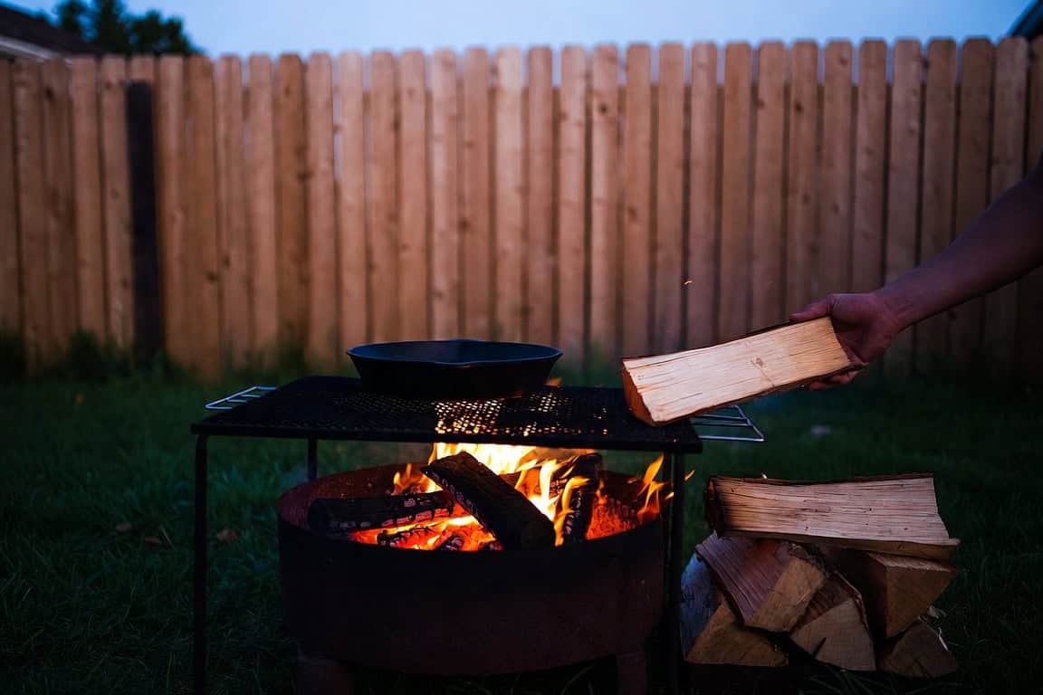 A steady fire in a fire ring with a skillet on the grate, being fed a fresh log