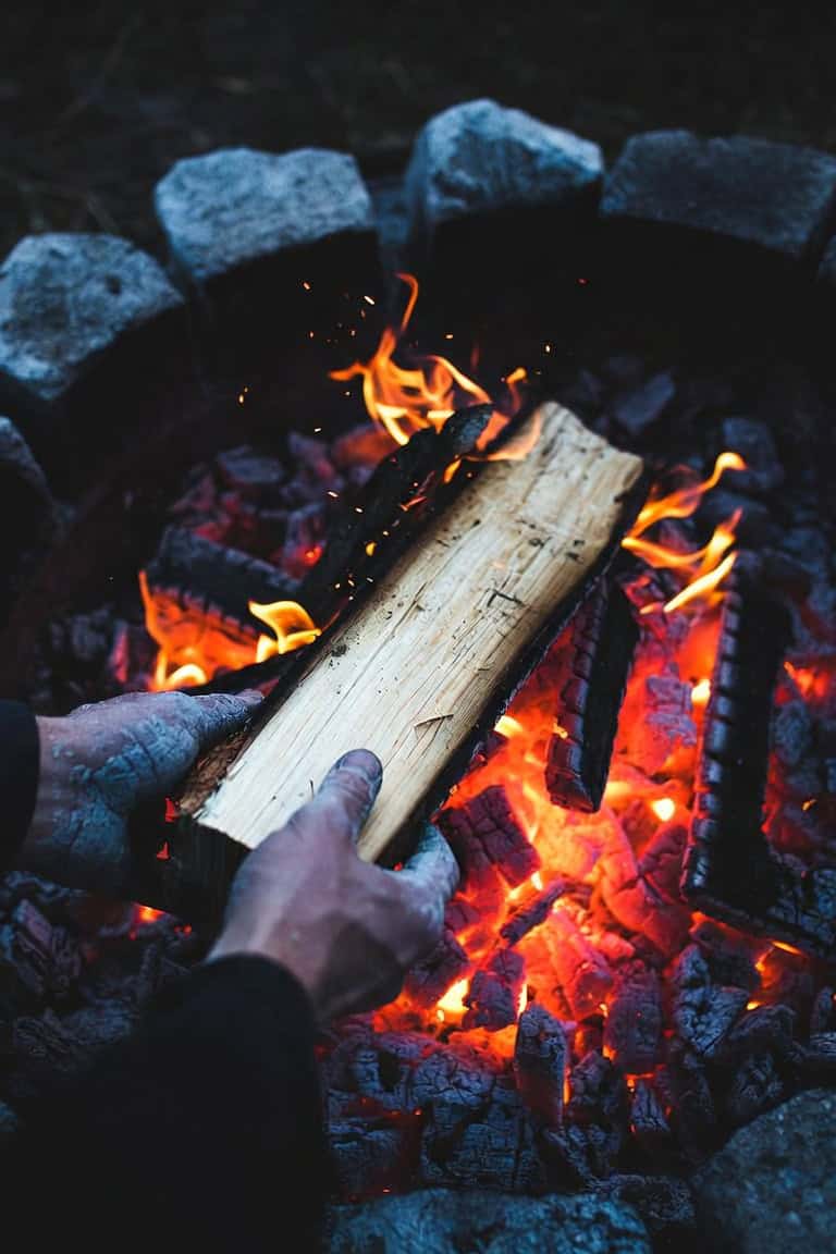 Hands placing a split log onto a bed of glowing coals